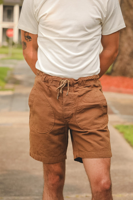 Person wearing brown shorts and a white t-shirt with a blurred outdoor background