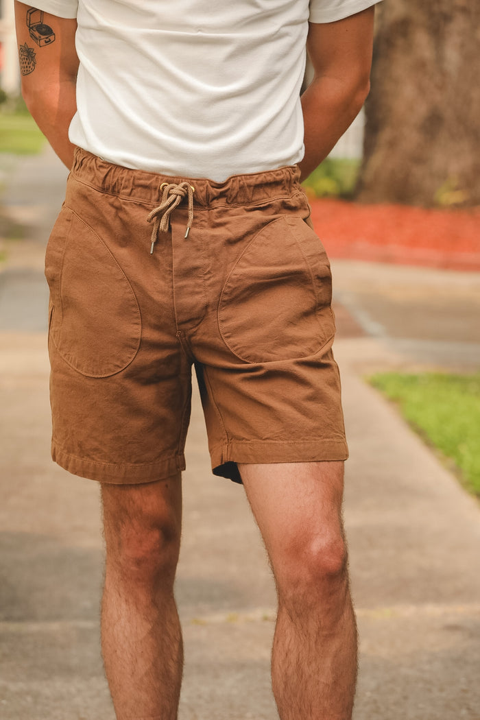 Person wearing brown shorts and a white shirt on a blurred outdoor background