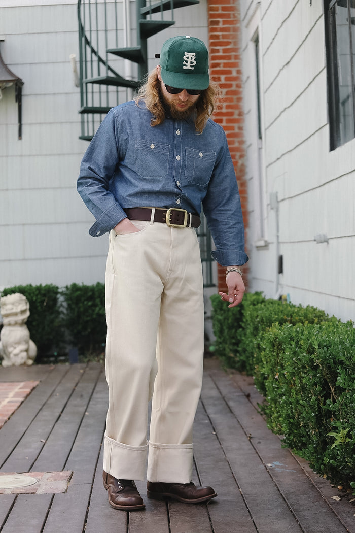 Person wearing a blue shirt, beige pants, and a green cap outdoors on a wooden deck.