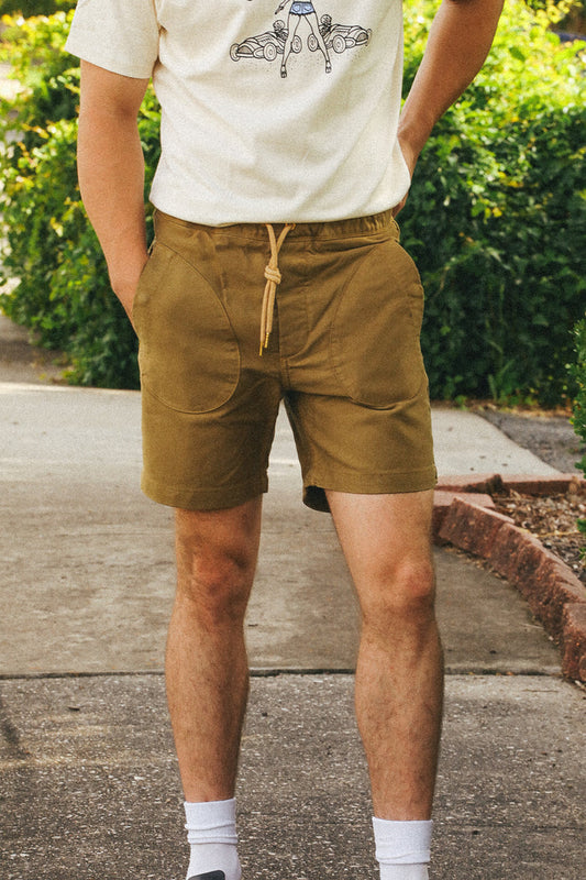 Person wearing a white t-shirt with a graphic design and brown shorts standing outdoors.