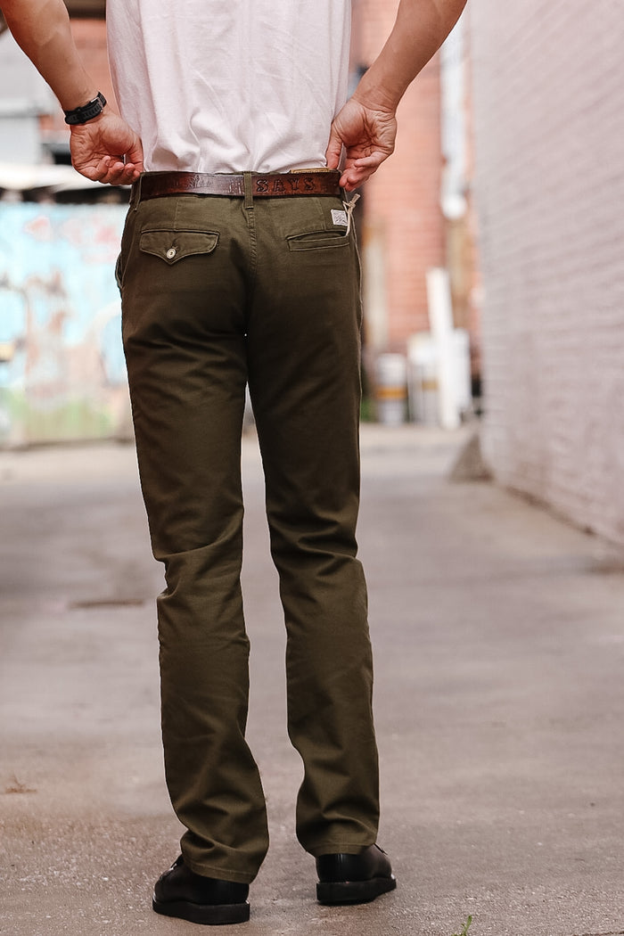 Person wearing olive green pants and a white shirt on a blurred street background