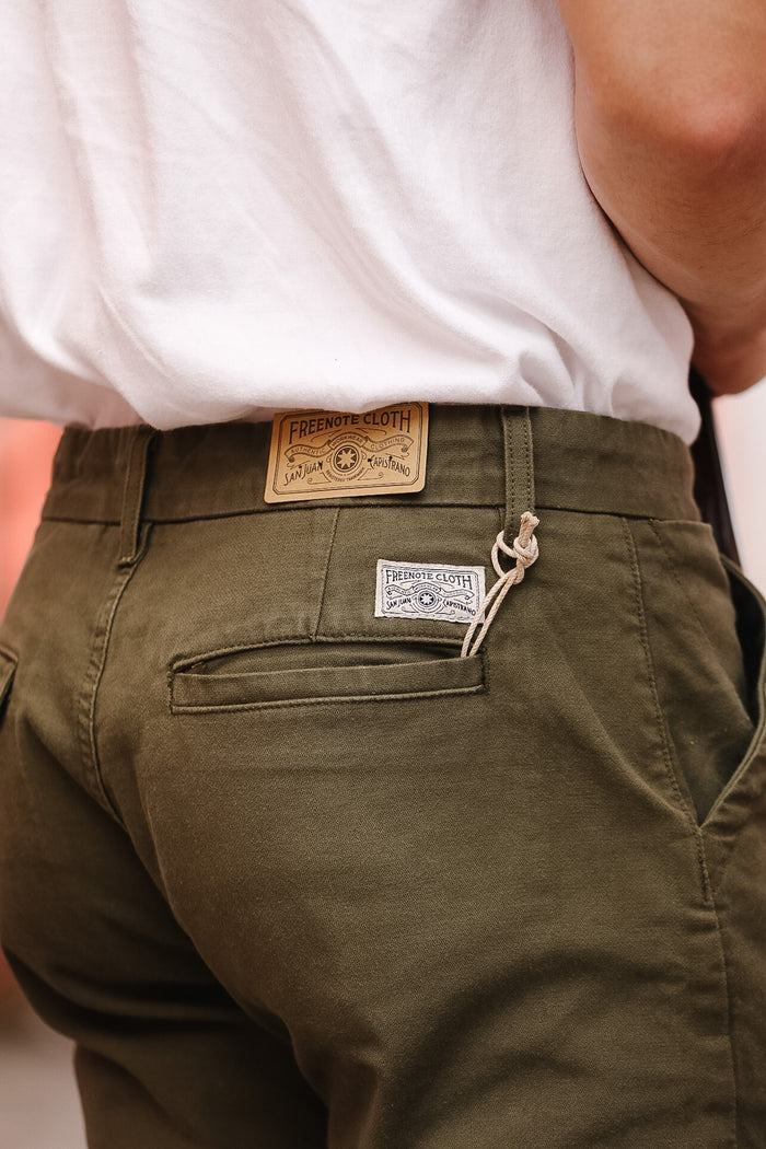 Green pants with brand labels on a neutral background