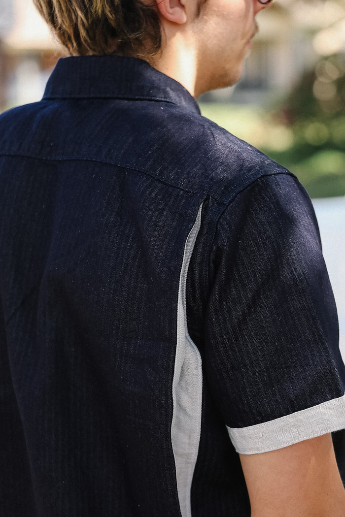 Person wearing a dark blue shirt with short sleeves and white trim, standing outdoors.