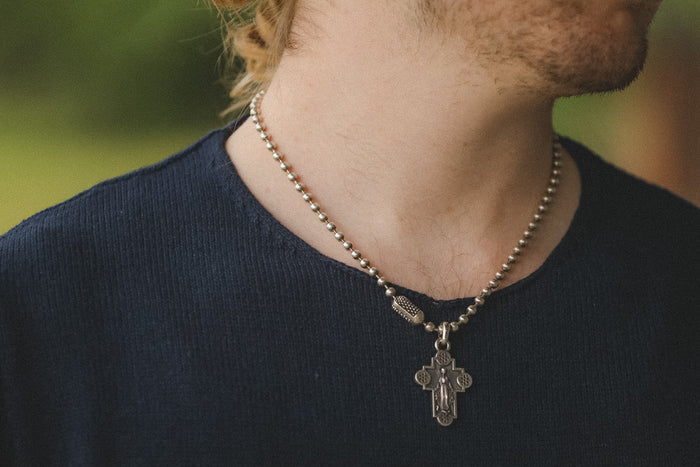 Person wearing a necklace with a cross pendant against a blurred natural background