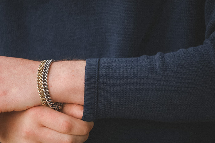 Close-up of a person wearing a gold chain bracelet on a dark sleeve.