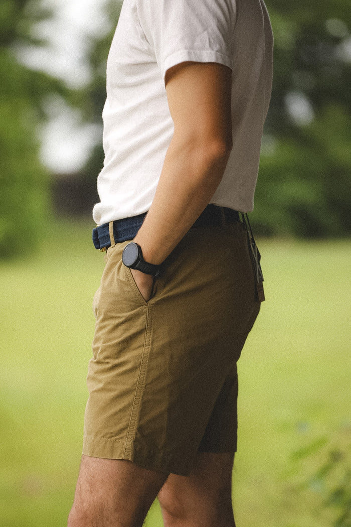 Person wearing a white t-shirt and brown shorts with a blurred green background