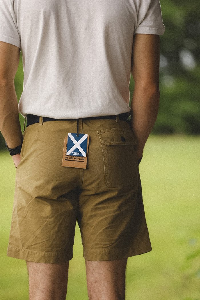 Person wearing brown shorts with a visible brand tag in an outdoor setting
