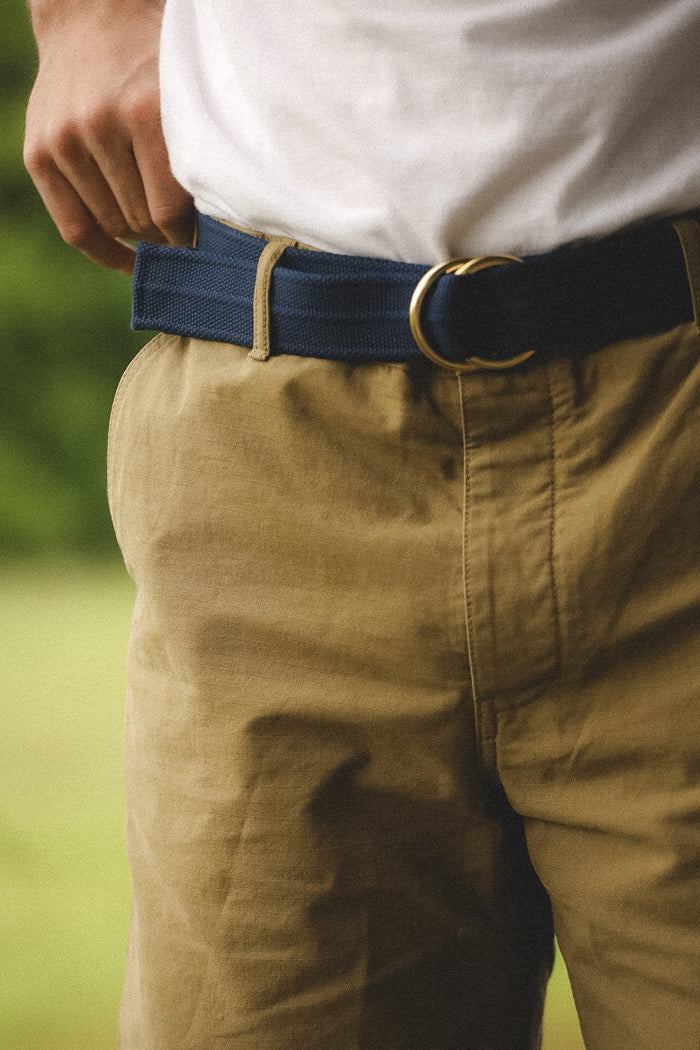Person wearing a blue belt with a gold buckle on beige pants against a blurred green background