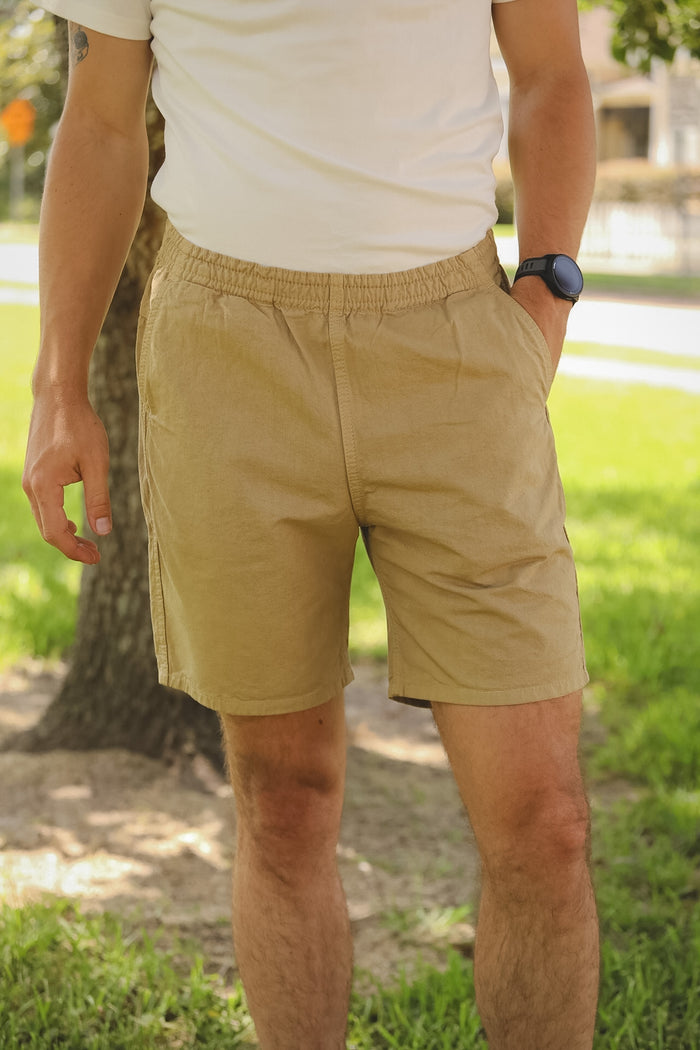 Person wearing beige shorts standing outdoors with grass and a tree in the background