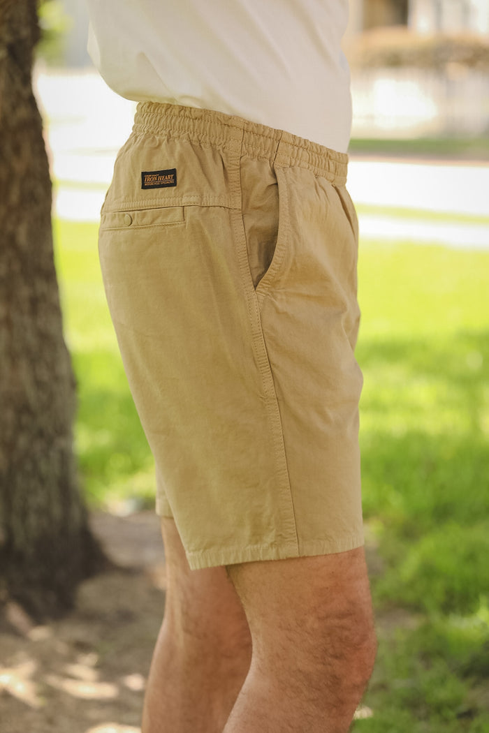 Beige shorts with a brand logo worn by a person in an outdoor setting.