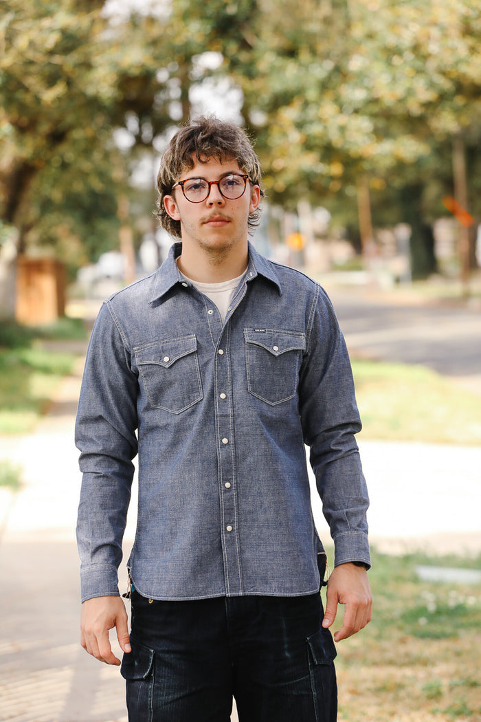 Person wearing a blue denim shirt outdoors with trees in the background