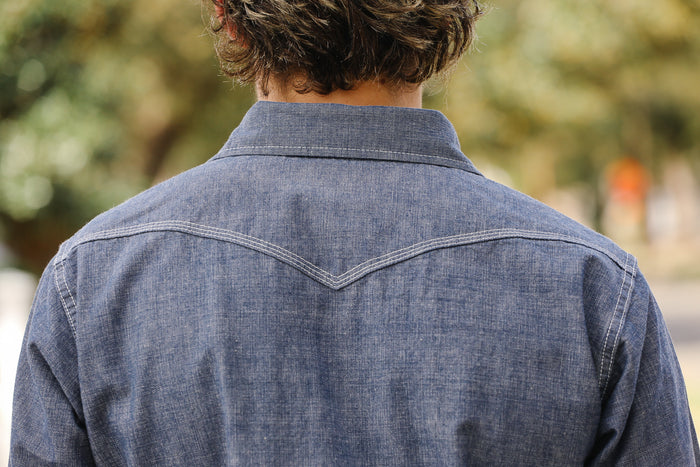 Person wearing a blue denim shirt with a blurred outdoor background