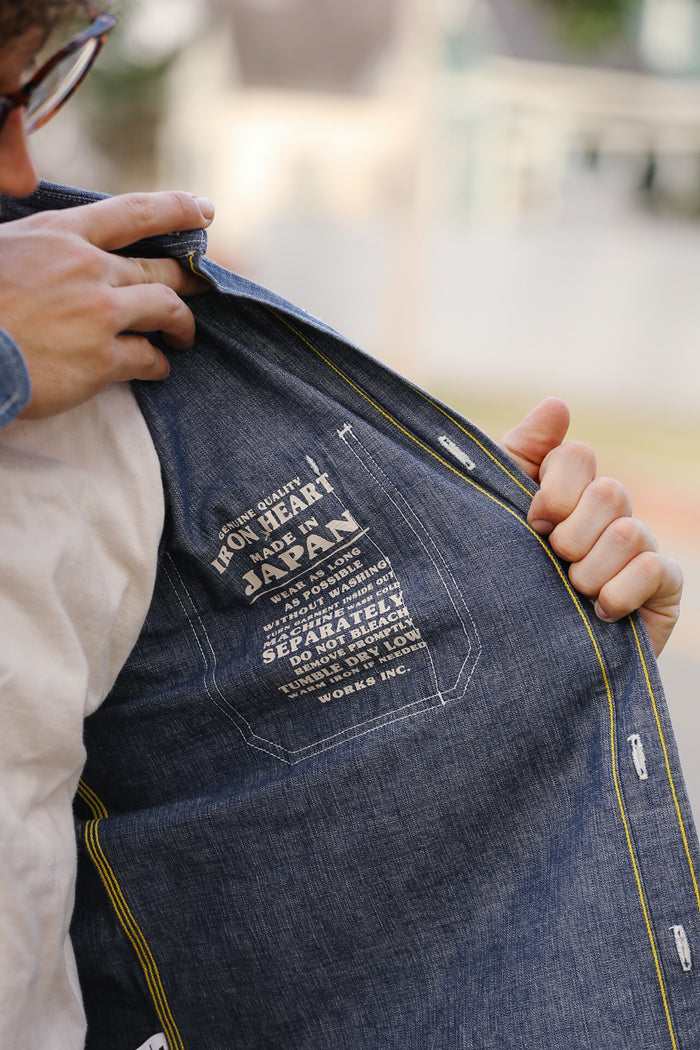 Person holding a denim jacket with branding details.