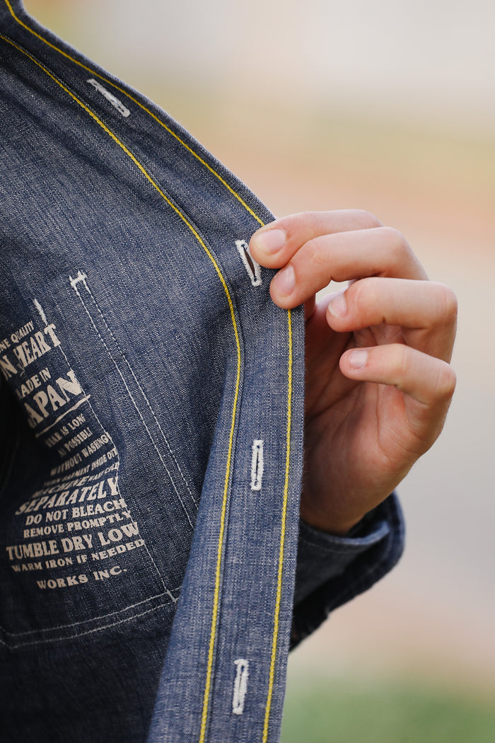 Close-up of a person adjusting the strap of a denim jacket with text on it.