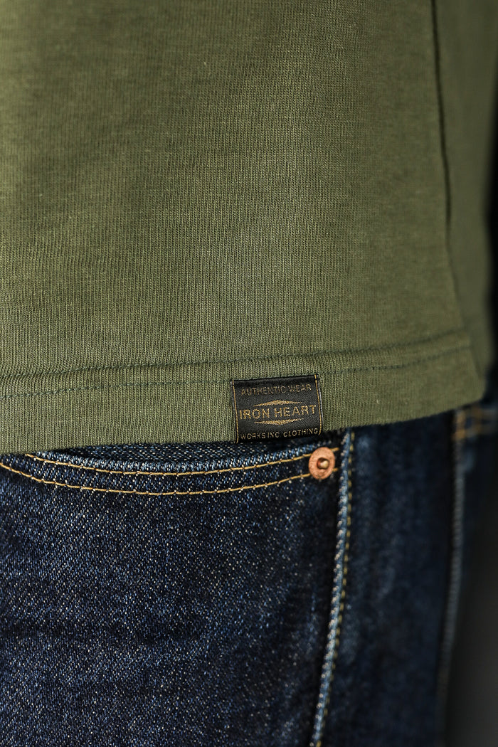 Close-up of olive green Iron Heart shirt tag above dark blue denim jeans with yellow stitching