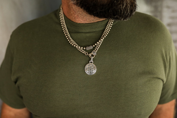 Close-up of man wearing layered silver chain necklaces with round pendant on green shirt
