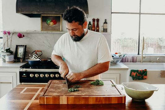 Man in white t-shirt chopping fresh greens on thick wooden cutting board in bright kitchen