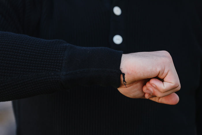 Close-up of a person wearing a dark sweater with a buttoned shirt underneath, holding their fist.