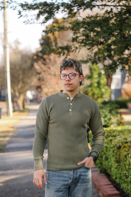 Person wearing a green long-sleeve shirt and glasses standing outdoors.