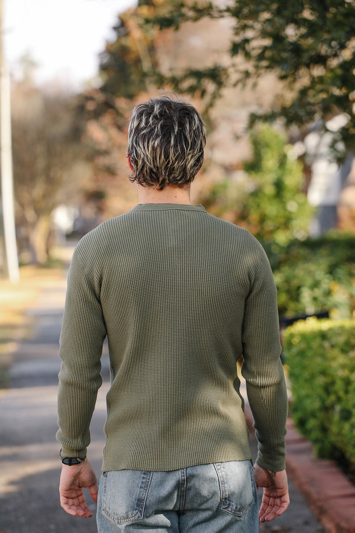 Person wearing a green sweater walking on a path with trees and bushes in the background