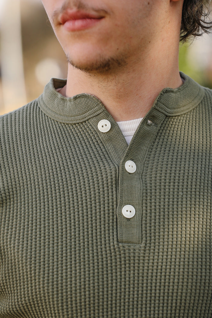 Close-up of a person wearing a green textured shirt with buttons.