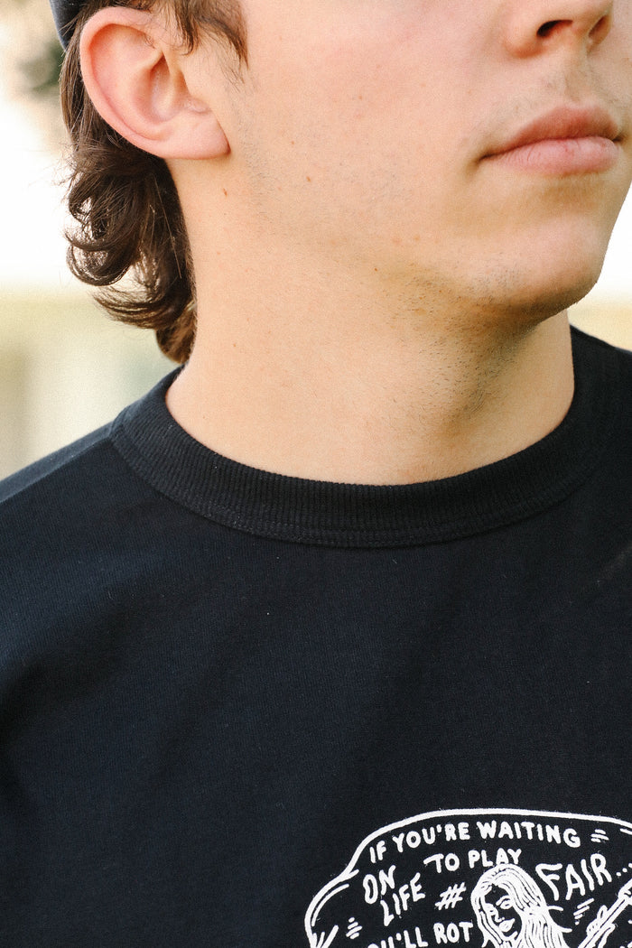 Close-up of man wearing black Iron Shop Provisions tee with white graphic text and illustration