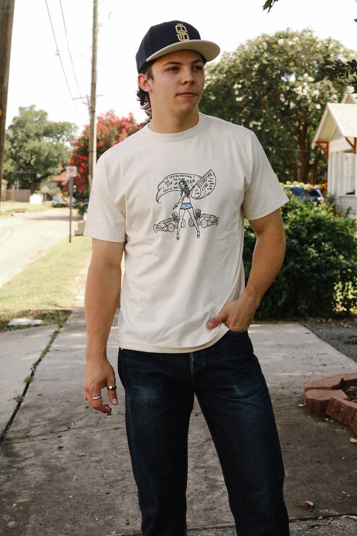 Man wearing cream Iron Shop Provisions Buffalo Nickel Starting Line Loopwheel tee and black cap standing on sidewalk