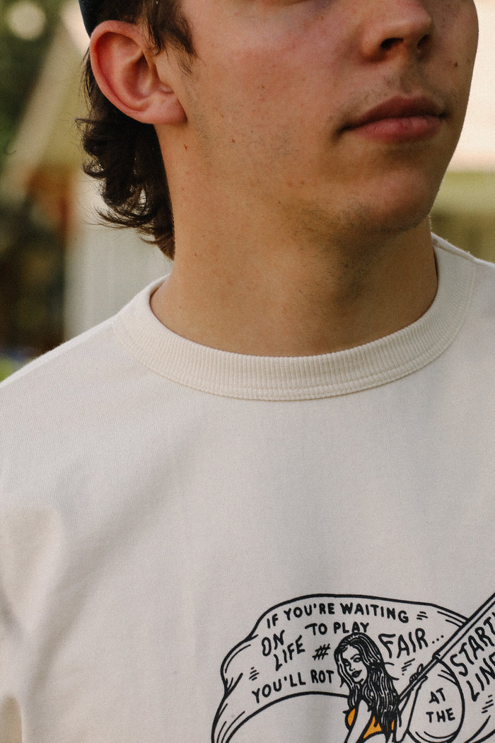 Close-up of a man wearing a cream ISP x Buffalo Nickel Starting Line Loopwheel T-shirt with graphic text