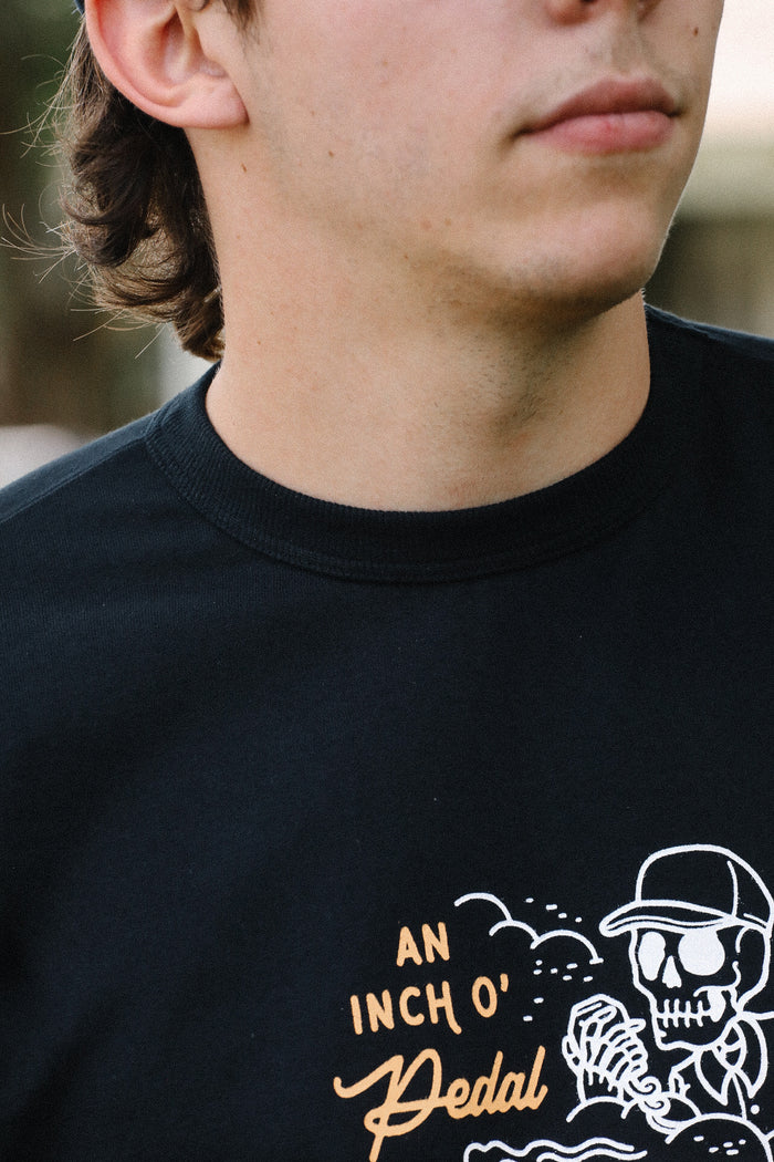Close-up of a man wearing a black Iron Shop Provisions tee with white skeleton and orange text graphic