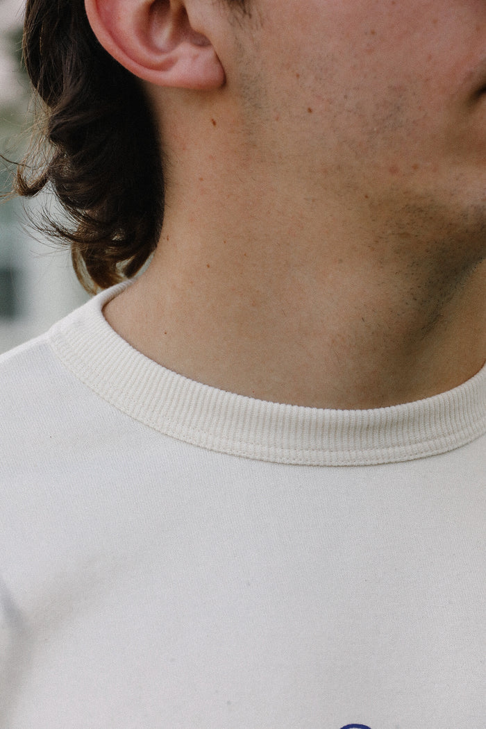 Close-up of a person wearing a cream loopwheel t-shirt from Iron Shop Provisions with visible neckline and textured fabric