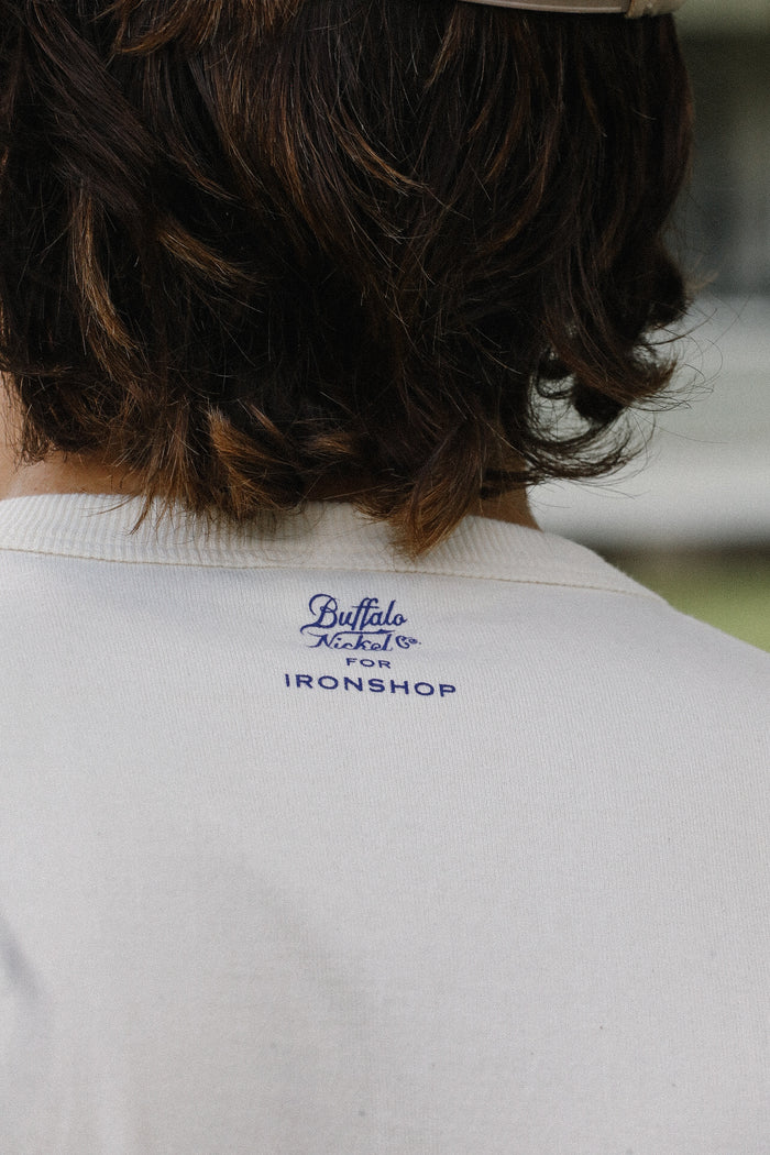 Close-up of cream loopwheel tee back with Buffalo Nickel Co logo for Ironshop under brown wavy hair