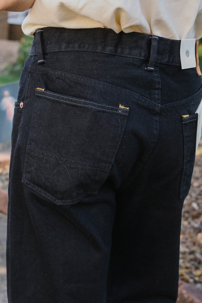 Close-up of black jeans with visible stitching and a fabric tag, worn with a light shirt outdoors