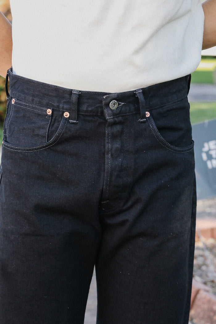 Close-up of person wearing black denim jeans with copper rivets and button fly from Iron Shop Provisions
