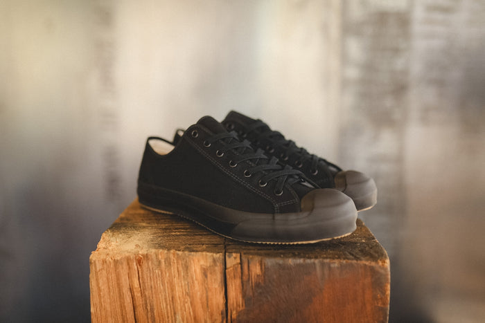 Up close image of a black sneaker on a wood block with a grey background