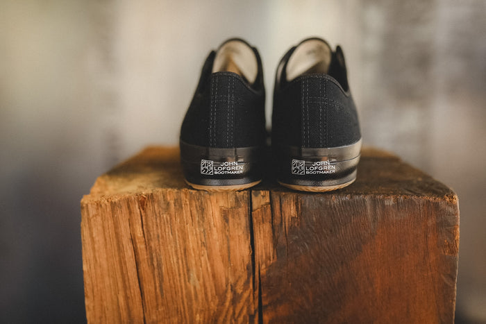 Up close image of a black sneaker on a wood block with a grey background