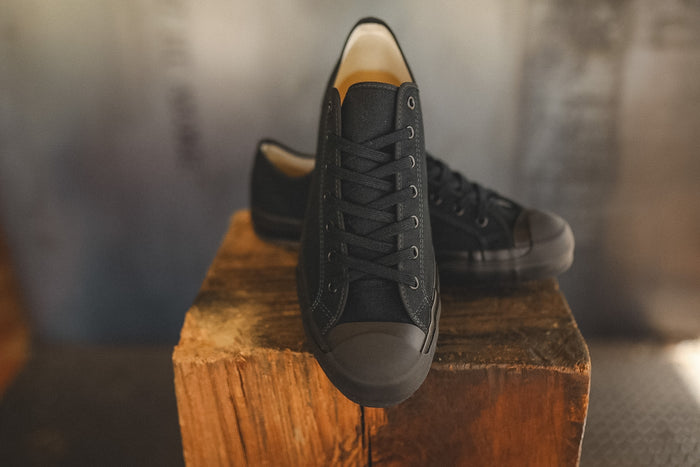Up close image of a black sneaker on a wood block with a grey background