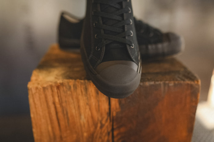 Up close image of a black sneaker on a wood block with a grey background