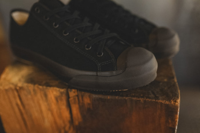 Up close image of a black sneaker on a wood block with a grey background
