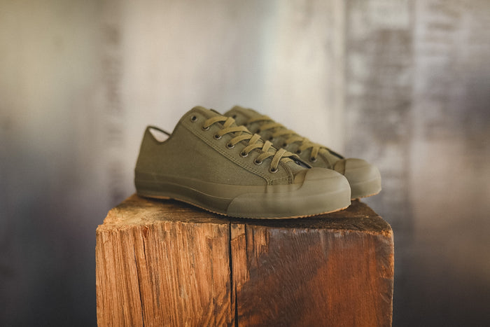 Up close image of a olive green sneaker on a wood block with a grey background