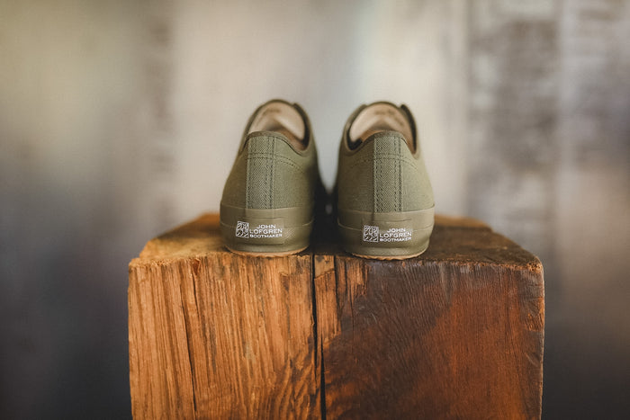 Up close image of a olive green sneaker on a wood block with a grey background