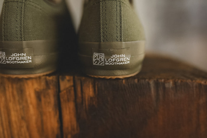Up close image of a olive green sneaker on a wood block with a grey background