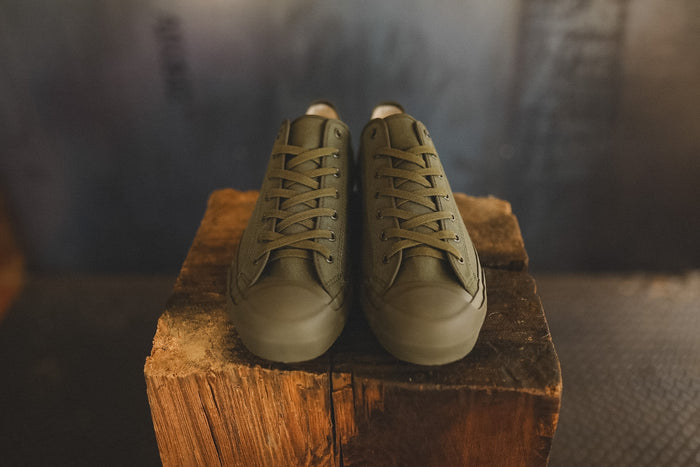 Up close image of a olive green sneaker on a wood block with a grey background