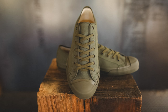 Up close image of a olive green sneaker on a wood block with a grey background