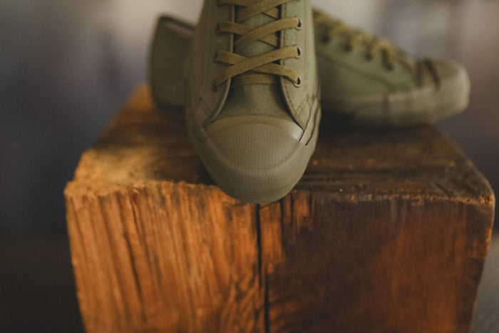 Up close image of a olive green sneaker on a wood block with a grey background