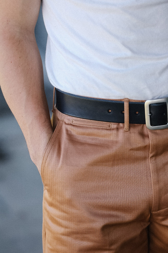 Person wearing a light blue shirt and brown pants with a black belt.