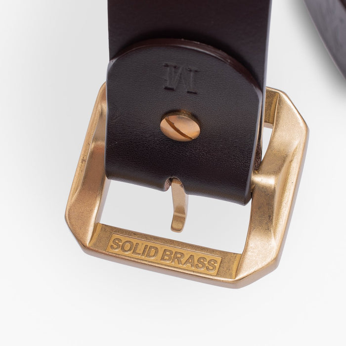 Close-up of black leather belt with solid brass buckle and engraved text on buckle