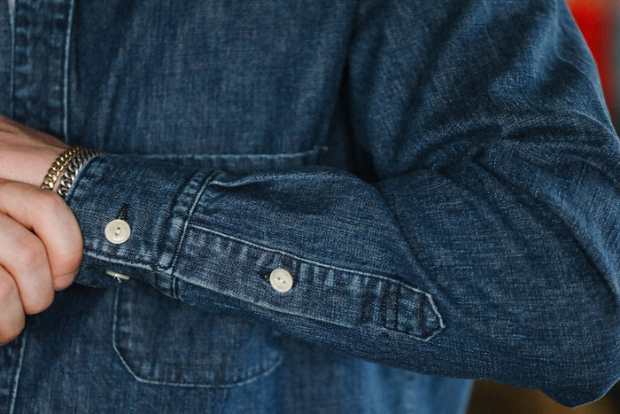 Close-up of person wearing a dark denim shirt with white buttons and silver bracelets on wrist