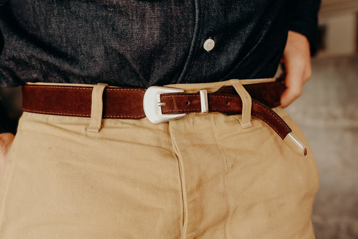 Close-up of brown leather belt with silver buckle worn with beige pants and dark denim shirt