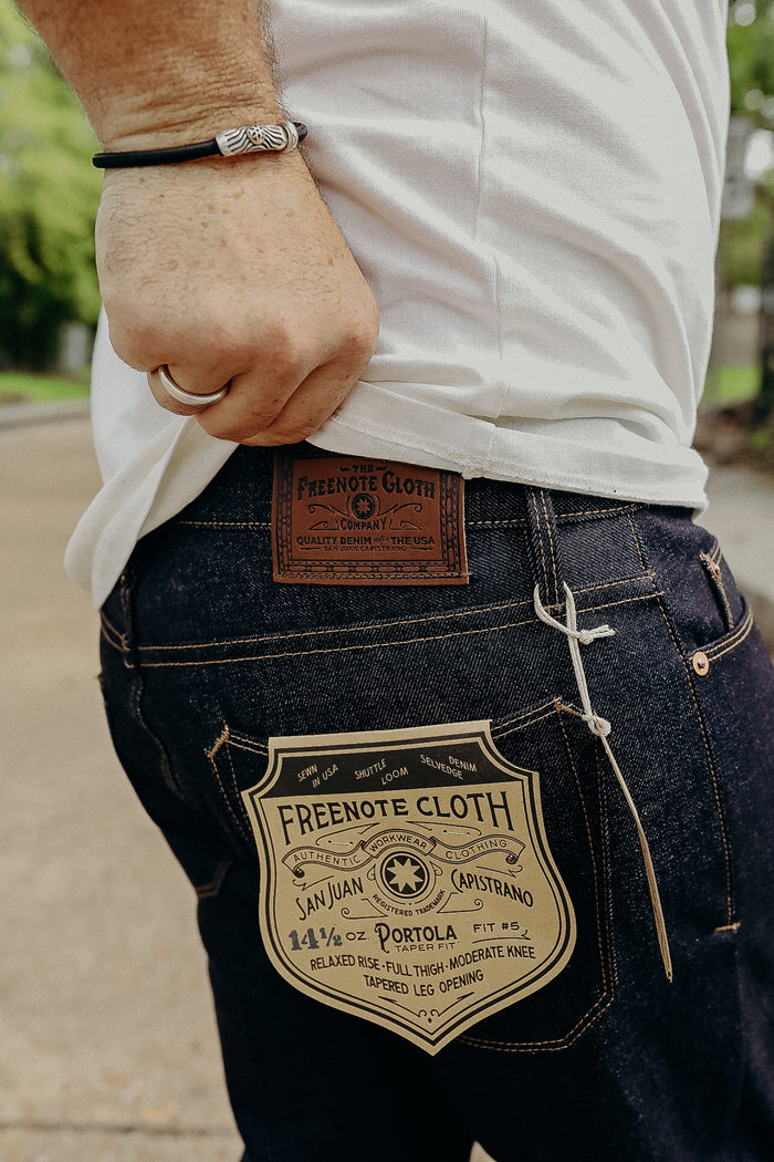 Close-up of person wearing Freenote Cloth dark denim jeans with label and white t-shirt outdoors