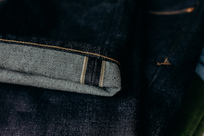 Close-up of dark raw selvedge denim jeans with visible cuff and orange stitching